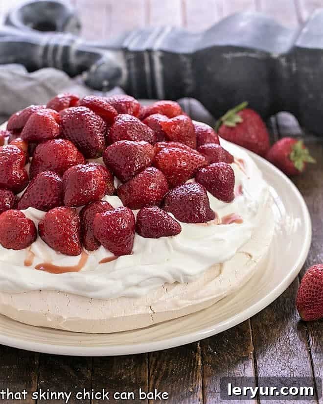 Strawberry Pavlova - A large 'squidgy' meringue shell topped with a pillow of whipped cream and balsamic strawberries Strawberry Pavlova on a white serving plate topped with halved strawberries and whipped cream.