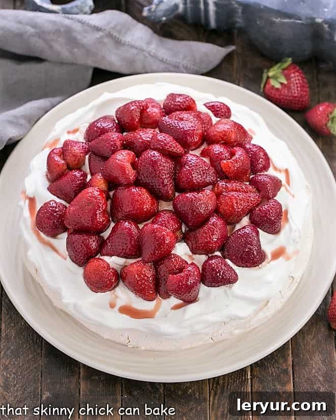 Strawberry Pavlova Recipe - A large 'squidgy' meringue shell topped with a pillow of whipped cream and balsamic strawberries Overhead view of a Strawberry Pavlova on a white serving plate.
