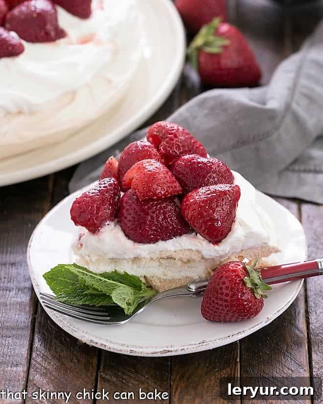 Strawberry Pavlova Dessert - A large 'squidgy' meringue shell topped with a pillow of whipped cream and balsamic strawberries Slice of strawberry pavlova on a dessert plate garnished with fresh mint.