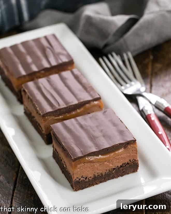 Three decadent Milky Way Brownies artfully arranged on a white ceramic tray, showcasing their rich layers.