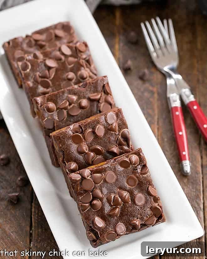 Overhead view of slices Caramel Brownies on a white rectangular tray with a couple of red handled forks, highlighting their rich texture.