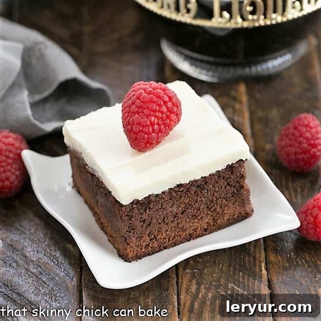 A raspberry brownie topped with cream cheese frosting and a fresh raspberry on a white plate, a delightful sight.
