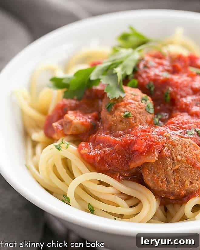 Close-up view of a rich homemade pasta sauce with sausage served over spaghetti in a white bowl, garnished with fresh herbs.