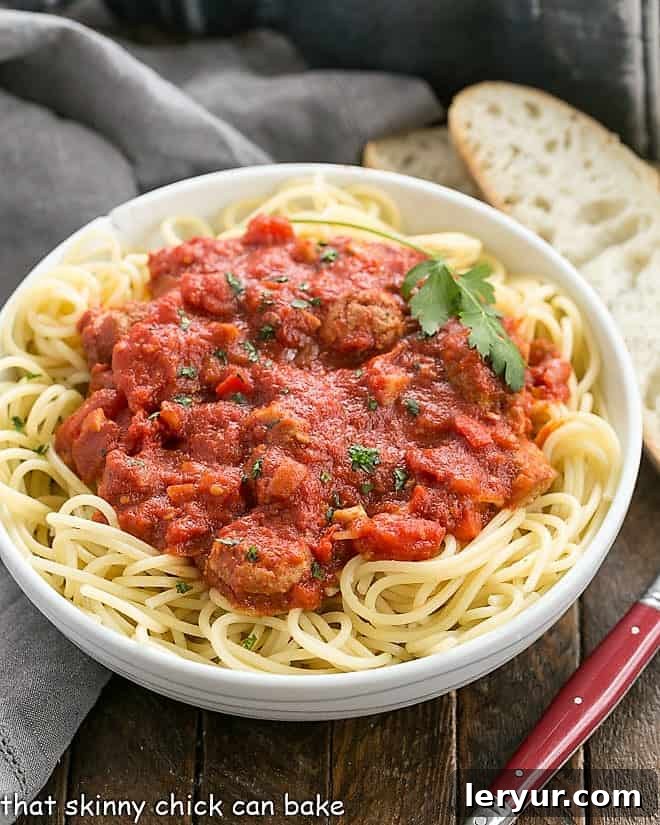 A bowl of spaghetti generously covered with homemade pasta sauce, accompanied by two slices of crusty bread and a fork, ready for a comforting meal.