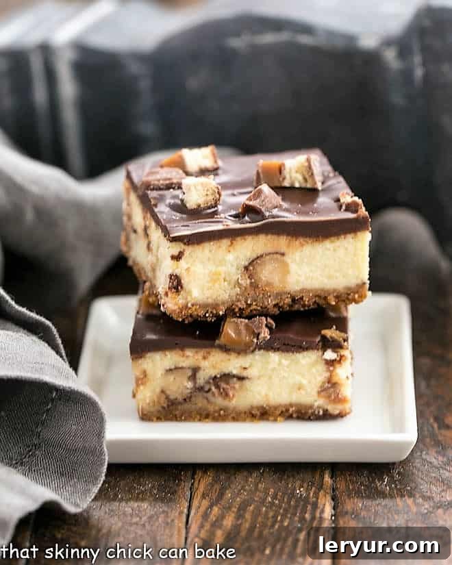 Twix Cheesecake Bars - when two favorite desserts collide! Twix bars, cheesecake plus ganache will dazzle your taste buds!! Two glistening Twix Cheesecake Bars stacked on a square white plate, ready to be enjoyed.