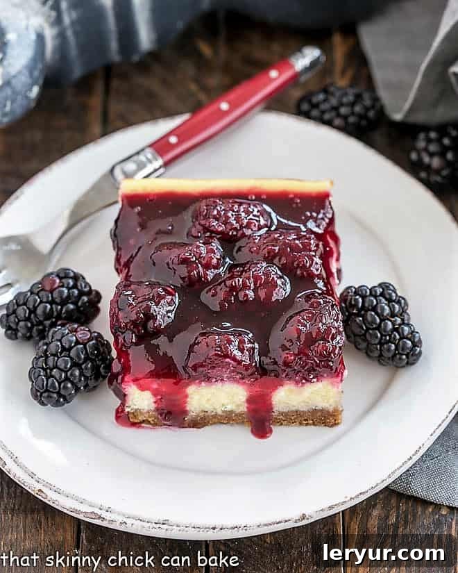 Blackberry Cheesecake Bars with a vanilla wafer crust, dreamy cheesecake filling and a fresh berrry topping making a delightful afternoon snack or dessert Delightful Blackberry Cheesecake Bars on a round white plate with fresh blackberries and a red handled fork, highlighting the creamy texture and vibrant fruit.