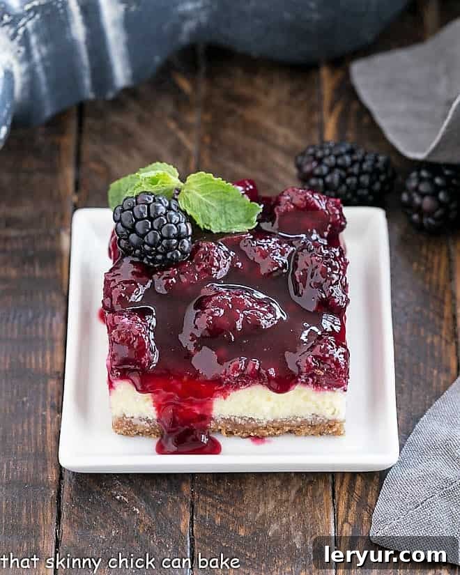 Blackberry Cheesecake Bars with a vanilla wafer crust, dreamy cheesecake filling and a fresh berrry topping making a delightful afternoon snack or dessert Single Blackberry Cheesecake Bar with Berry Topping on a square white plate, garnished with a fresh sprig of mint, showcasing its enticing layers.