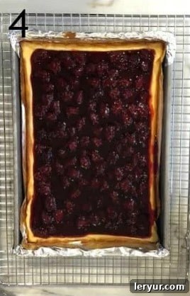 Blackberry Cheesecake Bliss Bars 5 Lustrous blackberry topping being spread over the cooled cheesecake layer in a pan, creating a vibrant finish.