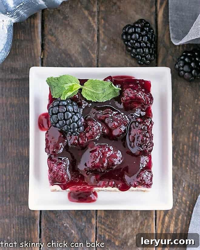 Best Cheesecake Recipe with a vanilla wafer crust, dreamy cheesecake filling and a fresh berrry topping making a delightful afternoon snack or dessert Overhead view of a perfectly sliced blackberry cheesecake bar on a square white plate with a sprig of mint, showcasing its beautiful layers.