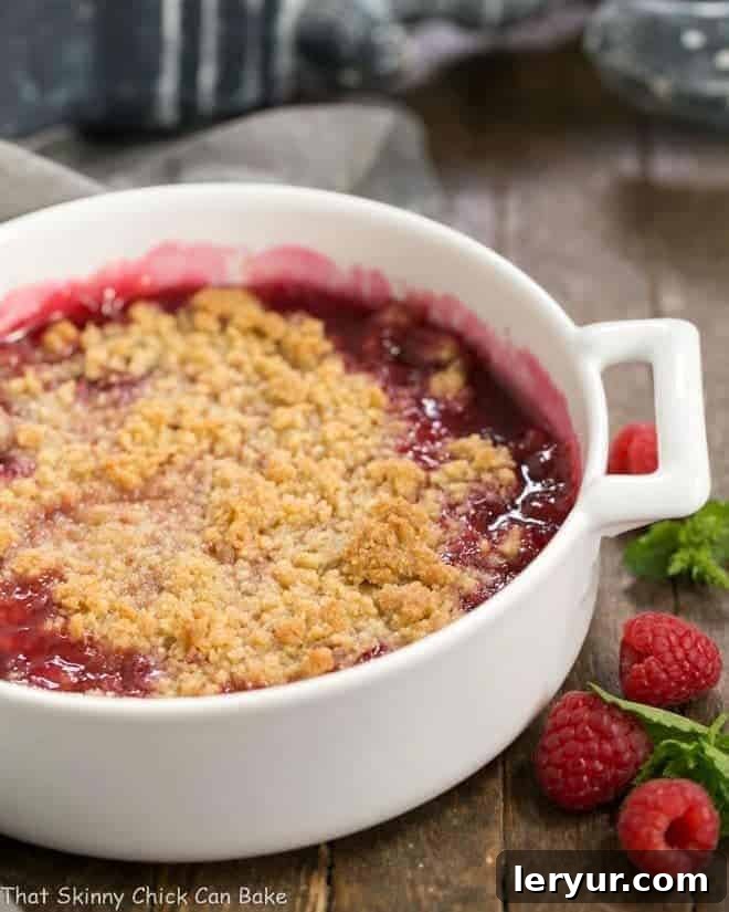 A round white casserole dish filled with a bubbling fresh raspberry crisp, topped with golden streusel.