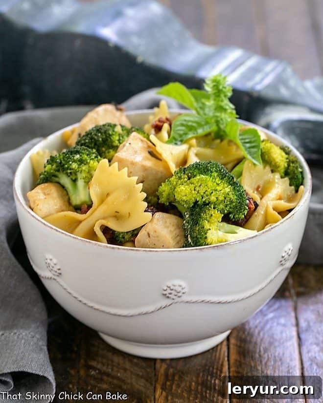 A ceramic bowl brimming with chicken, broccoli, sun-dried tomatoes, and bow tie pasta.