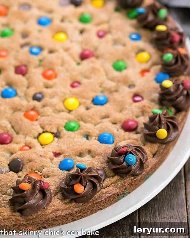 A close-up view of a festive chocolate chip cookie cake, studded with colorful M&M's.