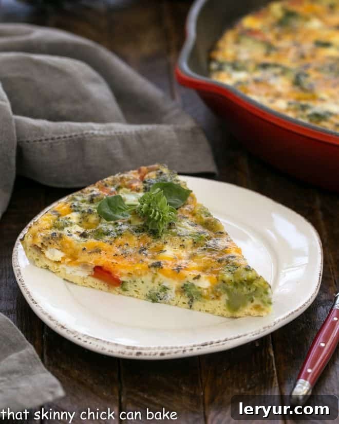 A perfectly portioned slice of roasted broccoli frittata on a white plate, with the red cast iron pan visible in the background.