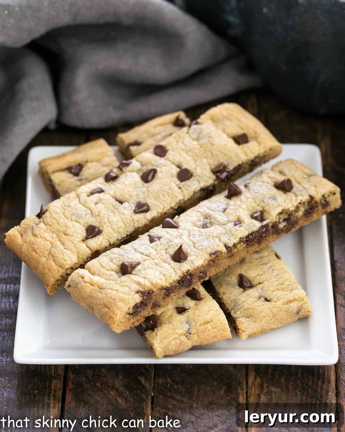 Four golden-brown chocolate chip cookie sticks arranged neatly on a pristine white square plate, showcasing their delightful texture and abundant chocolate chips.