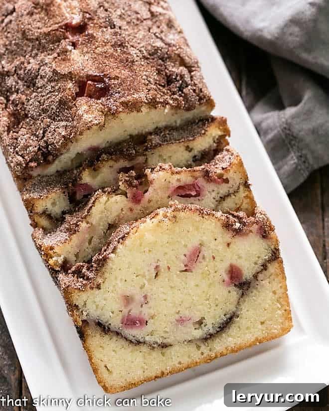 A delicious loaf of Cinnamon Swirl Rhubarb Bread on a white platter, showcasing its moist texture and cinnamon swirl.