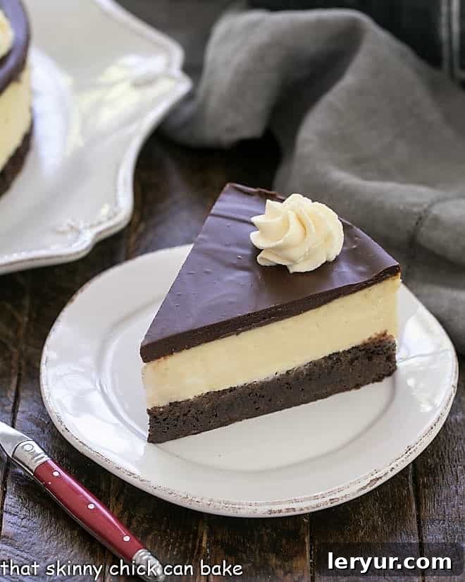 Slice of Baileys Brownie Cheesecake on a white dessert plate with a red handle fork, showing the thick ganache and whipped cream.