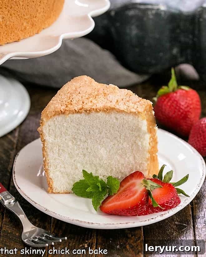 The Best Angel Food Cake Recipe - A detailed guide for baking this light and fluffy cake from scratch, complete with expert tips for perfect results. A perfect slice of angel food cake on a white dessert plate, elegantly topped with vibrant sliced strawberries and a sprig of fresh mint.