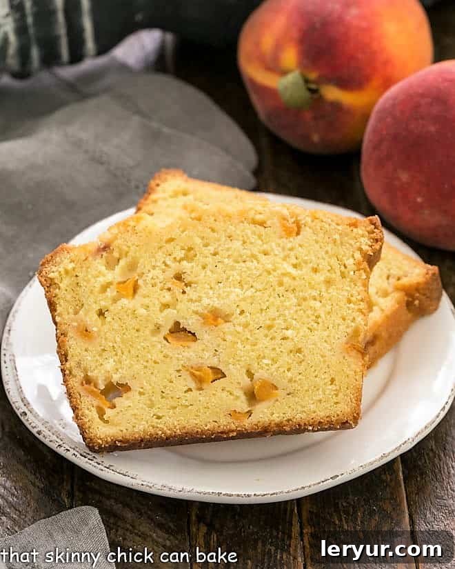 A stunning homemade Glazed Peach Pound Cake, enriched with peach puree and generous chunks of chopped peaches, creating an irresistible summer dessert perfect for any occasion. Two generous slices of glazed peach pound cake artfully arranged on a pristine white dessert plate, with the soft blur of fresh, whole peaches in the background, hinting at the cake's key ingredient.