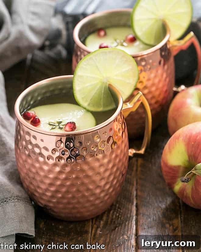 Cider Mules in shimmering copper mugs, garnished with vibrant lime wedges and thin apple slices, ready to be enjoyed.