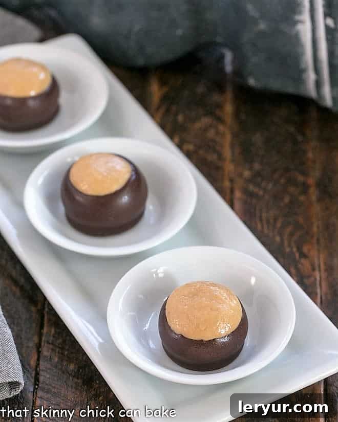 Buckeye Balls - AKA Buckeyes are an easy confection with only 6 ingredients! Reeses lovers will go crazy for these bon bons! Three perfectly dipped Chocolate Peanut Butter Balls displayed in small white dishes on a elegant white tray.