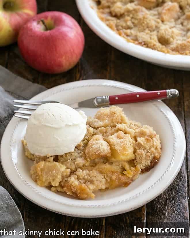 Golden Apple Crumble Served with Velvety Custard 3 Apple crumble with a scoop of ice cream on a white dessert plate.