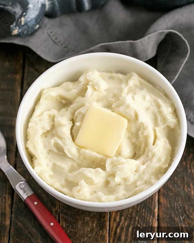 Overhead view of creamy mashed potatoes in a serving bowl, garnished with fresh herbs.