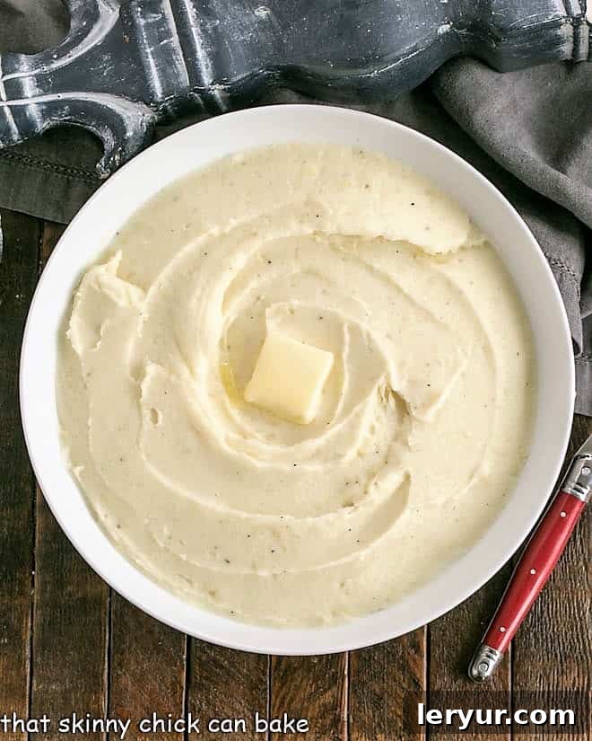 Overhead view of a serving bowl of mashed potatoes with a pat of butter melting in the middle.