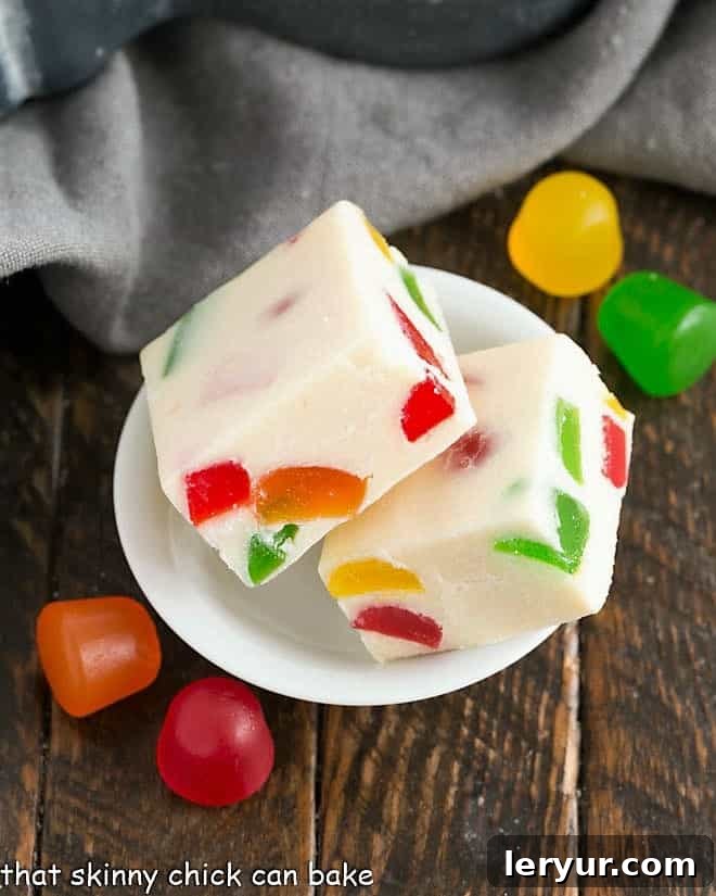 Two squares of white chocolate fudge in a small white bowl, showcasing their vibrant gumdrop inclusions.