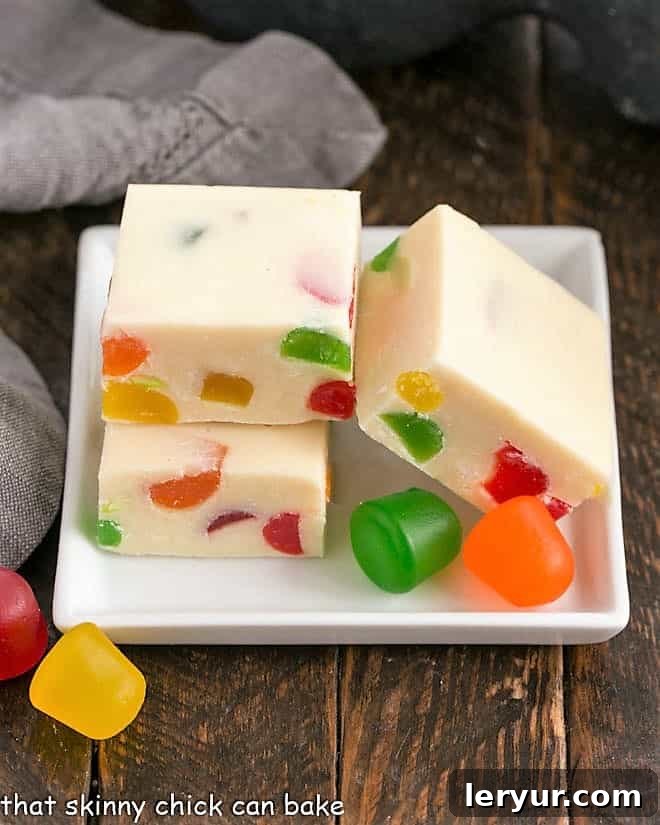 3 cubes of festive white chocolate fudge on a square white plate garnished with gumdrops, highlighting their festive colors.