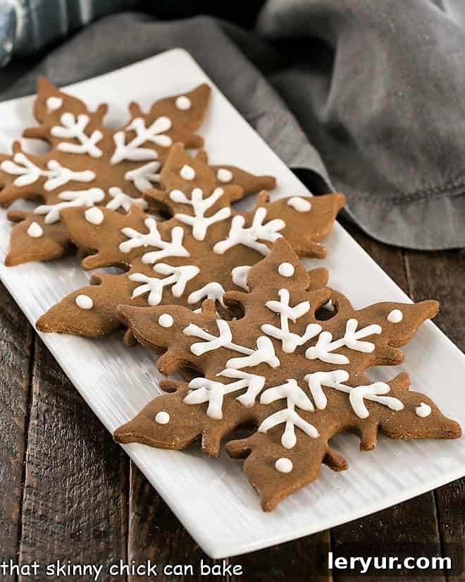 Three perfectly baked gingerbread snowflakes arranged artfully on a pristine white platter, showcasing their intricate details and festive charm.