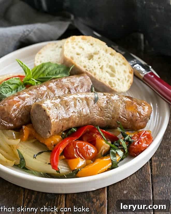 Sheet Pan Sausage and Peppers - a roasted version of an Italian-American classic that concentrates the flavor and deliciousness! Serve straight up or in buns for a comforting meal. A serving of Sheet Pan Sausage and Peppers on a white dinner plate, accompanied by a slice of rustic bread and a red-handled fork. The roasted vegetables and sausage are perfectly cooked and appealing.