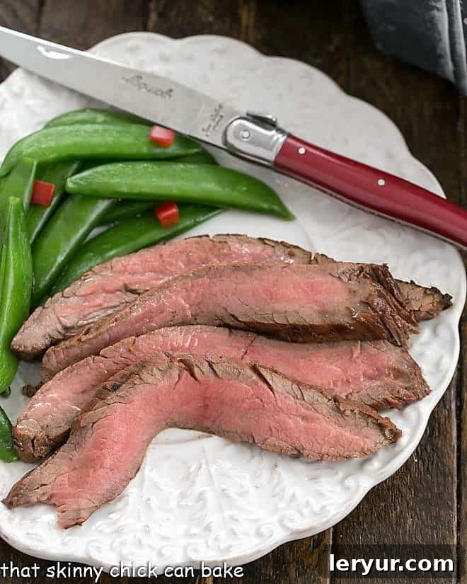 Overhead view of slices of flank steak, sugar snapped peas and a red handle knife.