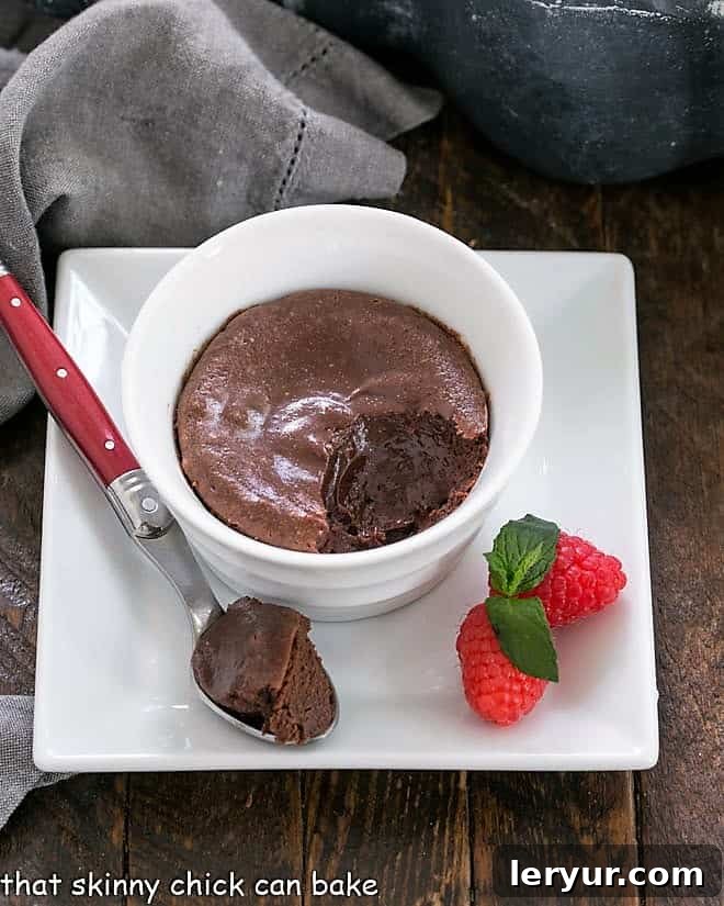 Individual chocolate cheesecake in a white ramekin on a square white plate with a spoonful removed
