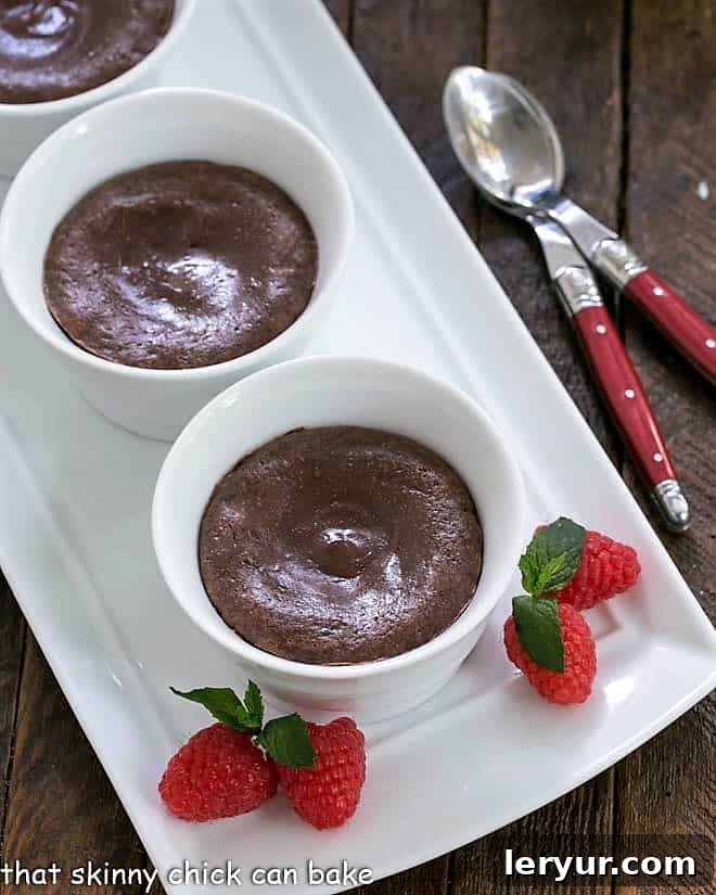 3 warm chocolate cheesecakes on a white tray with raspberries and mint.