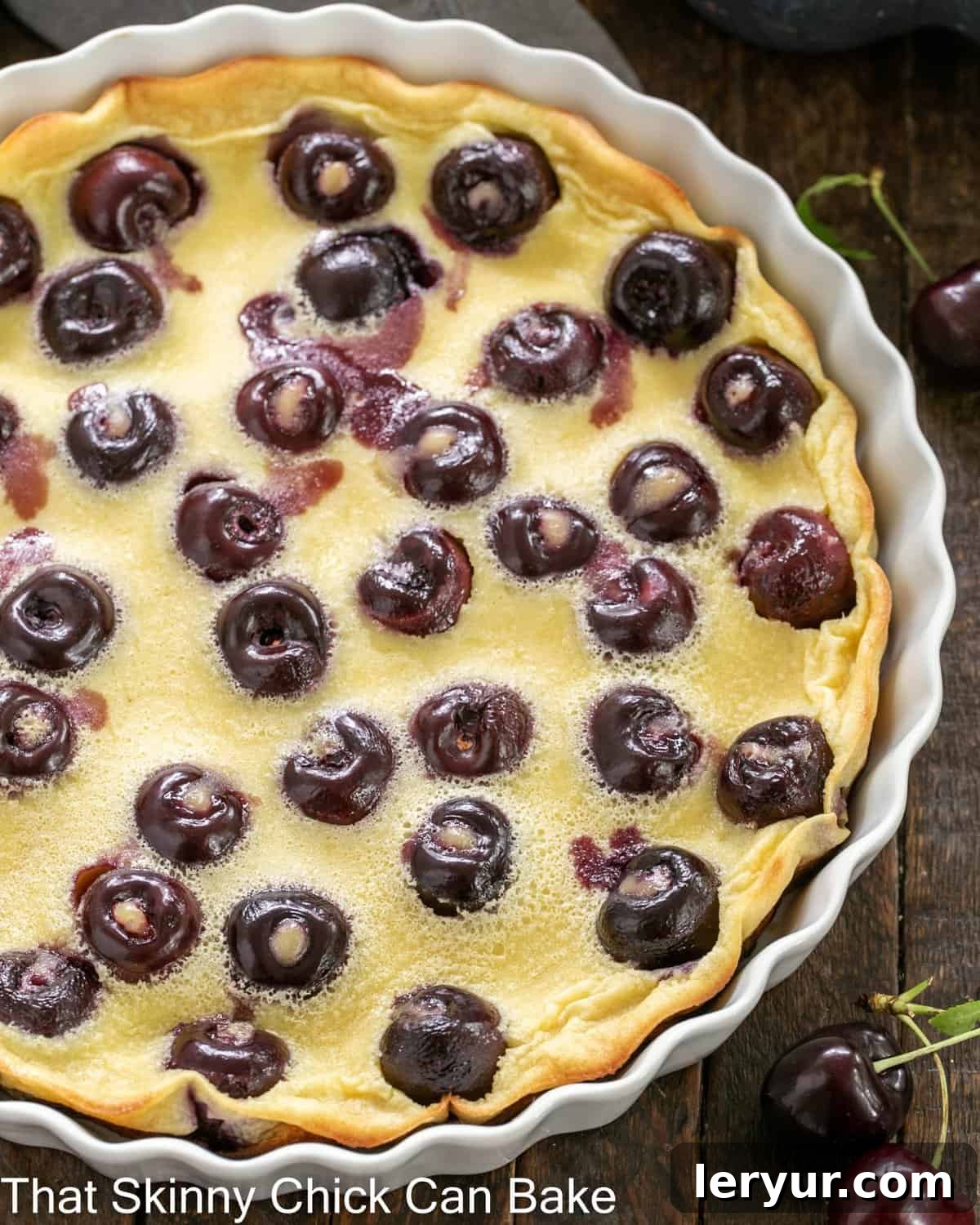 Whole-Cherry Clafoutis - A rustic French tart featuring cherries! Overhead view of a baked cherry clafoutis in a shallow white souffle dish, dusted with powdered sugar.