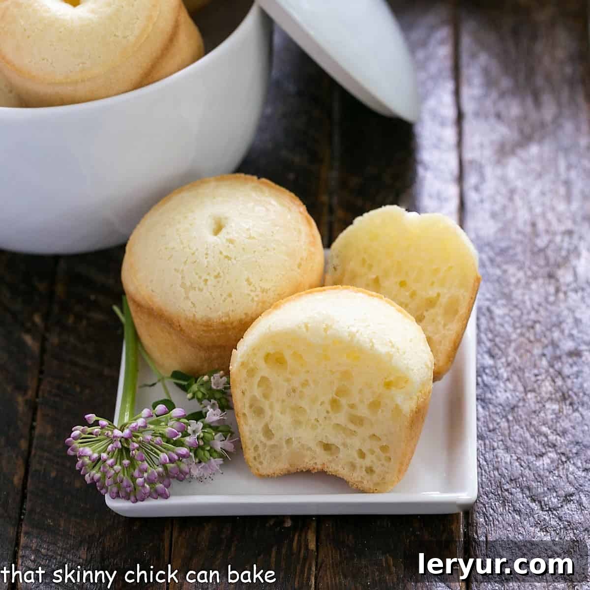 A freshly baked Brazilian cheesebread sliced open on a white plate, revealing its airy, chewy interior, garnished with a delicate chive flower.