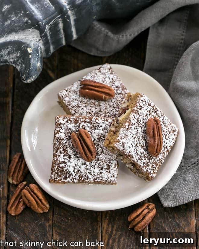 Three golden brown Southern Pecan Bars on a round white plate, generously dusted with powdered sugar, showcasing their rich, chewy texture.