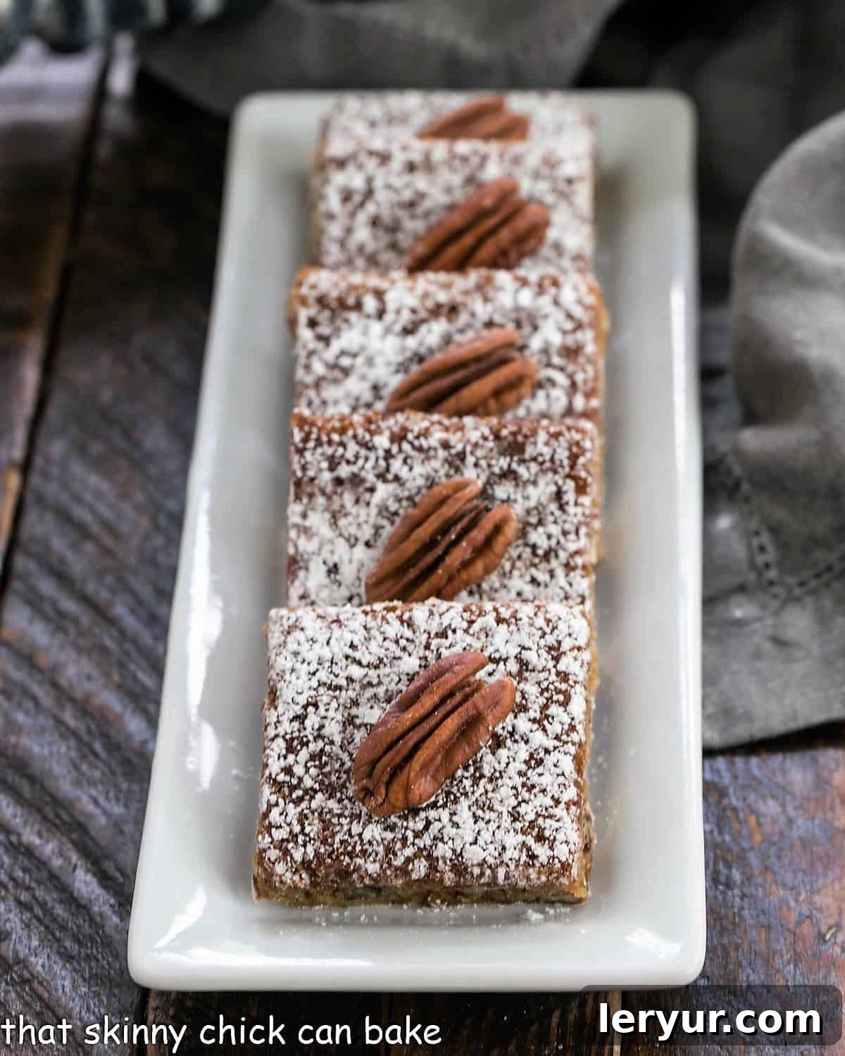 Rows of perfectly sliced Southern Pecan Bars, elegantly dusted with powdered sugar, arranged neatly on a white rectangular tray.