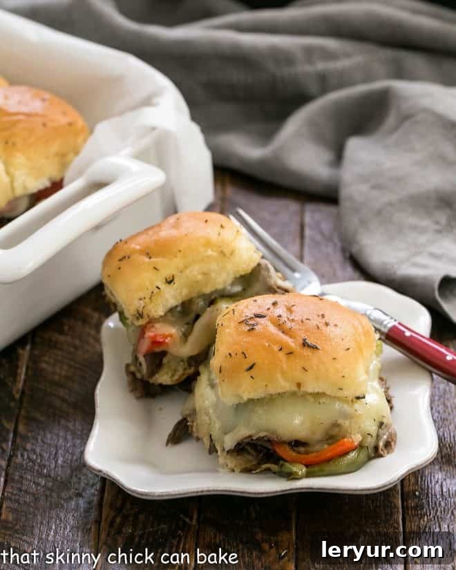 Two cheesy cheesesteak sliders on a white plate with a fork, ready to be eaten
