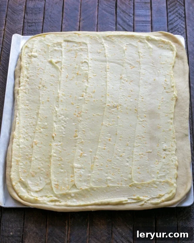 Half of the vibrant orange filling evenly spread across the rolled-out dough rectangle, ready for rolling.