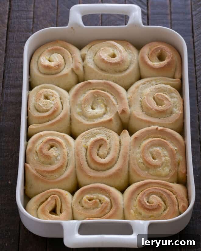 Freshly baked orange rolls in their baking dish, generously covered with a smooth, creamy orange frosting while still warm.