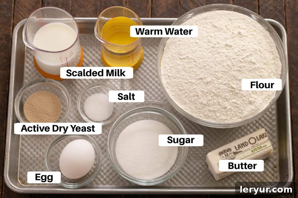 A neatly arranged collection of ingredients for homemade orange roll dough, including flour, sugar, butter, yeast, milk, water, egg, and salt, displayed on a sleek metal sheet pan.