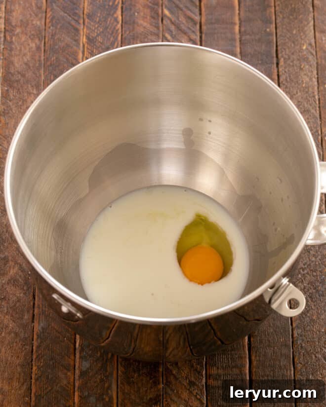 Milk, butter, and egg added to the mixer bowl, ready to be incorporated with the yeast mixture.