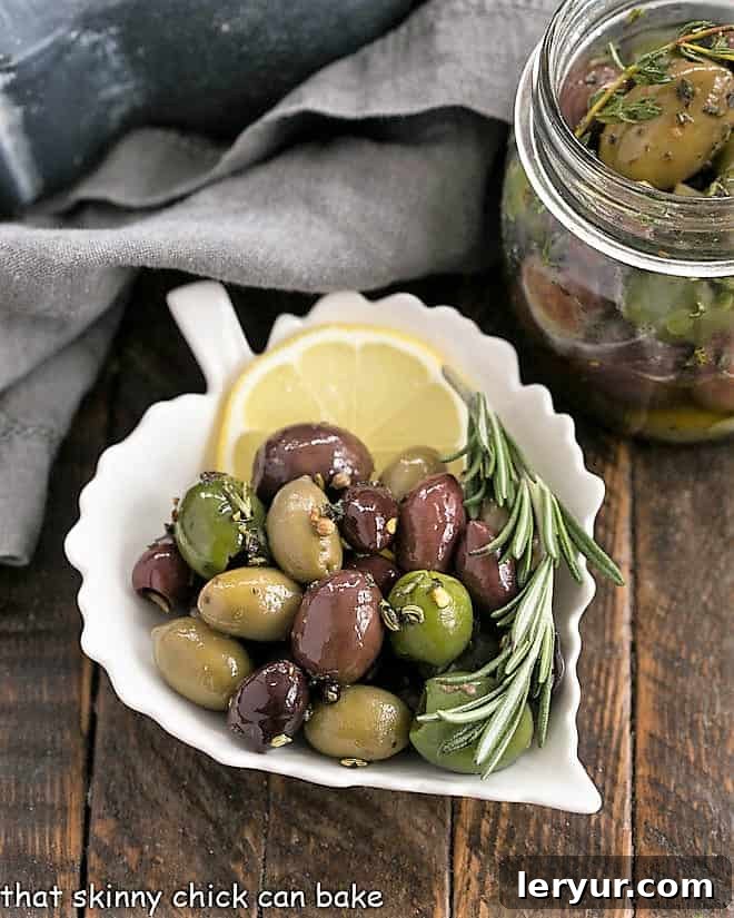herbed olives in a ceramic leaf plate with a slice of lemon and rosemary