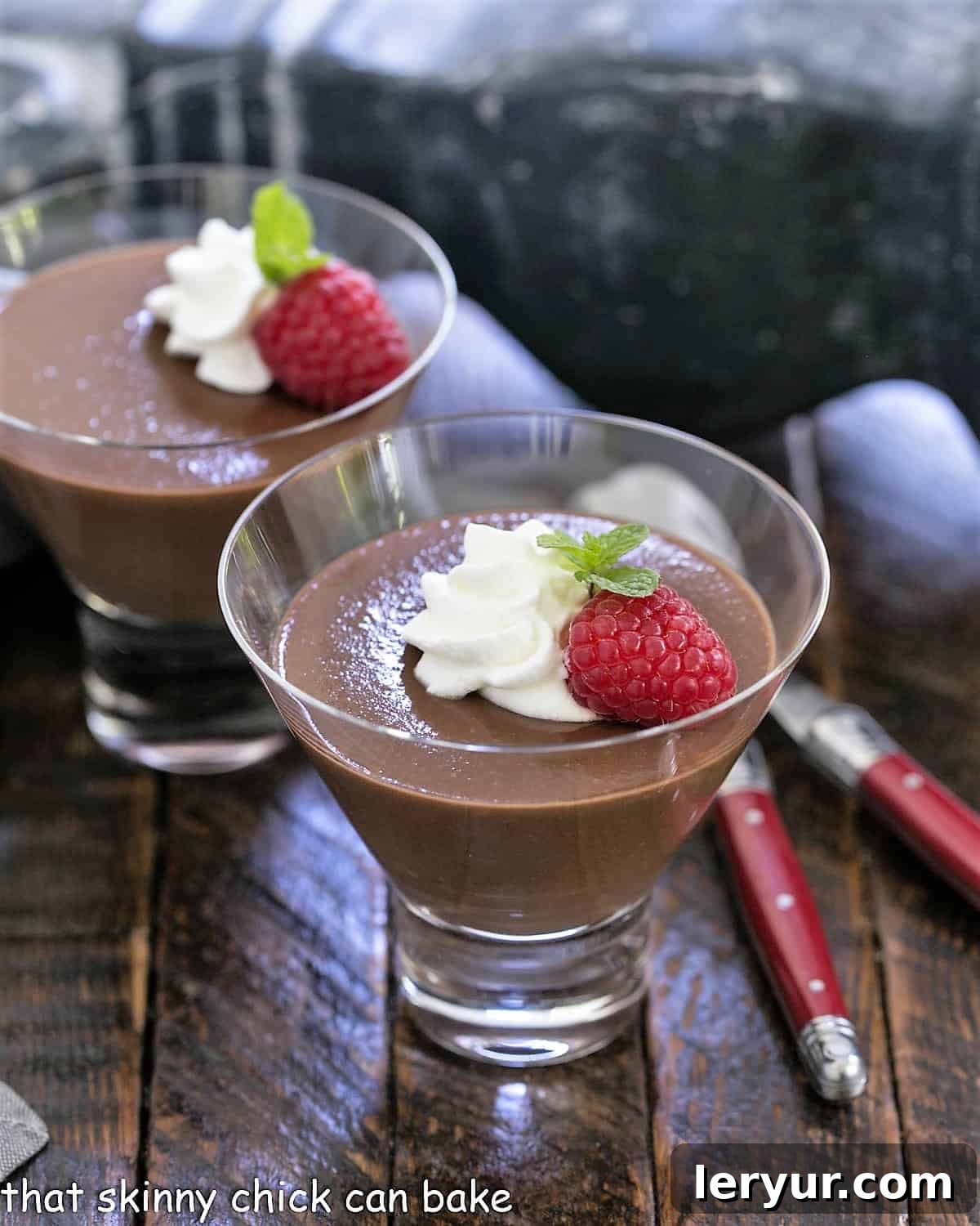 Decadent Italian Chocolate Budino 2 Two glass dishes showcasing rich Italian chocolate pudding, elegantly topped with fluffy whipped cream, vibrant red raspberries, and a fresh sprig of mint, ready to be savored.
