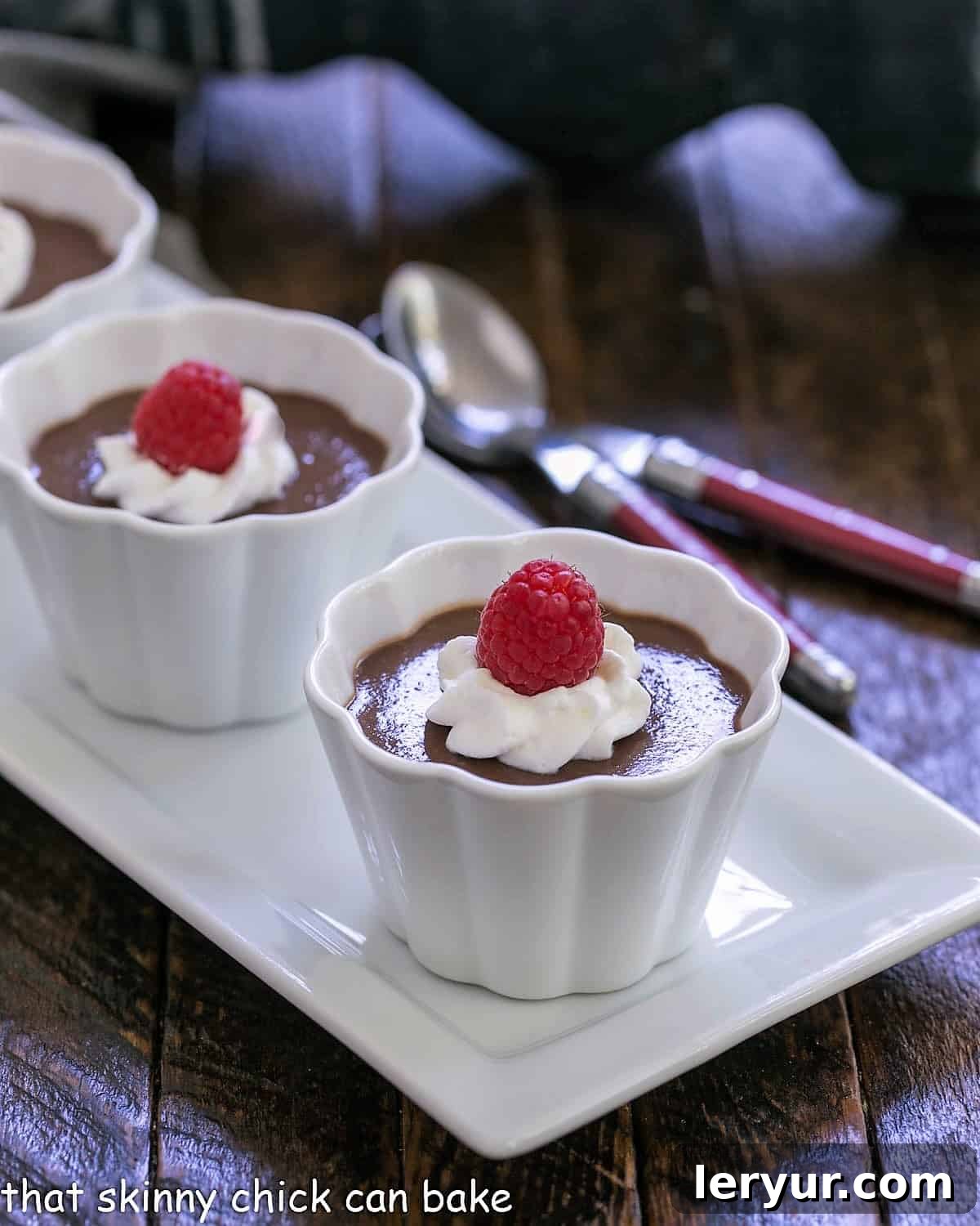 Decadent Italian Chocolate Budino 3 Three white ramekins filled with Italian chocolate pudding, each garnished with a swirl of whipped cream and fresh raspberries, presented beautifully.