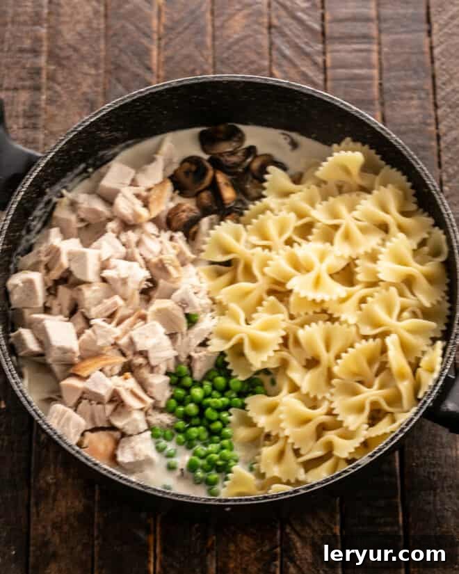 Creamy Homestyle Turkey Tetrazzini 5 Cooked pasta, bright green peas, savory mushrooms, and tender turkey pieces being folded into a creamy sauce in a large skillet.