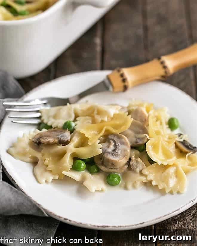 Delightful Turkey Casserole Recipe - A harmonious blend of comfort food with tender leftover poultry, vibrant peas, earthy mushrooms, and a dreamy cream sauce! A serving of Turkey Tetrazzini on a white plate with a bamboo handle fork, showcasing the creamy pasta, turkey, and peas.