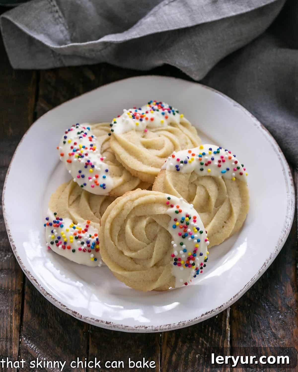 Delightful Danish butter cookies, elegantly dipped in white chocolate and adorned with festive sprinkles, arranged beautifully on a round white plate.