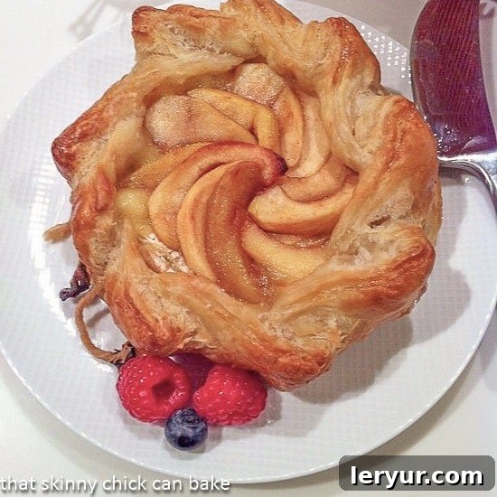 Baked Brie en croute with apples - an elegant appetizer that everyone will love! Apple Topped Baked Brie en Croute on a white serving plate, garnished with fresh rosemary